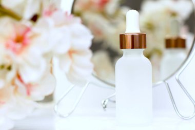 Beyaz çiçekli pipetli mat beyaz kozmetik şişesi ve ayna yansıması, cilt bakımı, kaplıca güzellik terapisi.