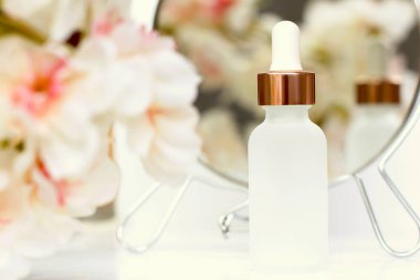 Beyaz çiçekli pipetli mat beyaz kozmetik şişesi ve ayna yansıması, cilt bakımı, kaplıca güzellik terapisi.