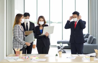 Takım elbiseli Asyalı bir işadamı, bir grup iş arkadaşına rastlarken maske takıyor. Ekip toplantı için hazırlanıyor. Coronavirüs salgını sırasında yeni normal ofis işi kavramı.