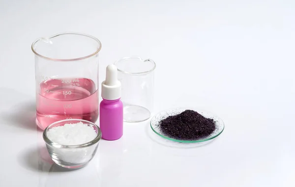 Cosmetic chemicals ingredient on white laboratory table. Potassium Permanganate Liquid, KMnO4, Serum bottle with dropper and Microcrystalline wax in glass container.