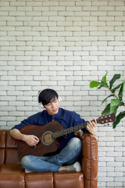 Beyaz kulaklıklı genç Asyalı adam gitar çalıyor oturma odasında dinleniyor, hafta sonunun keyfini çıkarıyor. Stressiz konsept