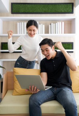 Genç aşıklar tatillerini birlikte oturma odasında geçirirler. İkisi de yumruklarını kaldırdı ve adam dizüstü bilgisayarını tutarken e-postayla aldıkları iyi habere sevinerek gülümsedi..