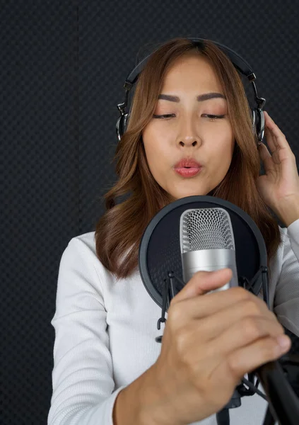 Musician producing music in professional recording studio. Young asian woman in white long sleeve t-shirt singing in front of black soundproof wall. (Close up)