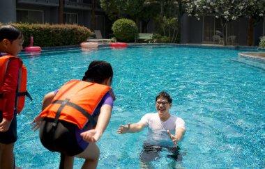 Asyalı bir baba ailesiyle havuza tatile çıkar ve suya atlayacak kızını yakalamaya hazırlanır..