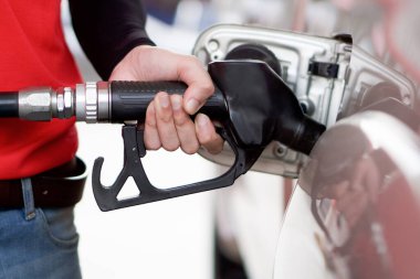 Kırmızı üniformalı benzin istasyonu çalışanı bronz kamyonet deposunu dolduruyor. Yakından bir el siyah benzin pompası hortumu tutuyor..