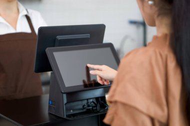 Genç Asyalı müşteri tezgahtaki bilgisayar monitöründen seçerek içecek menüsü sipariş ediyor. Önlüklü garson diğer tarafta emirlerinizi bekliyor..