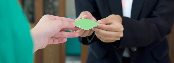 The hotel manager in black suit recieve a room card from the guest. Close up