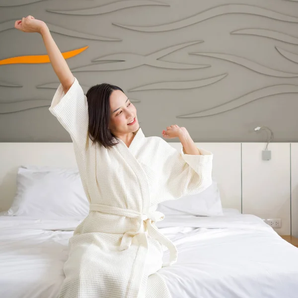 バスローブでアジアの女性の休暇中に残りの部分は ベッドで自宅に座っている 朝起きてからのストレッチ — ストック写真