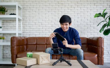 Genç Asyalı adam cep telefonuyla internet üzerinden deri kutuda güneş gözlüğü satıyor. Küçük ev işi konsepti.
