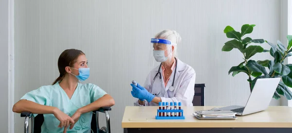 顔の盾と保護マスクを持つ老婦人医師は 車椅子に座っている患者に測定結果を温度に通知します 病院でのCovid 19試験 — ストック写真