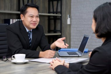 Siyah takım elbiseli Asyalı yönetici başvuru sahibini gülümseyerek sorguladı. Modern ofiste iş görüşmesi ortamı..