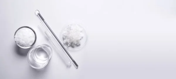 Crystal clear liquid in beaker, Microcrystalline wax in glass container, Flake salt in Chemical Watch Glass placed next to the Stirring Rod and Test tube. Chemicals ingredients on  laboratory table