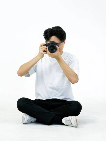 身穿白色T恤的年轻亚洲摄影师坐在白色摄影现场 透过取景器观看 照相馆的气氛 — 图库照片
