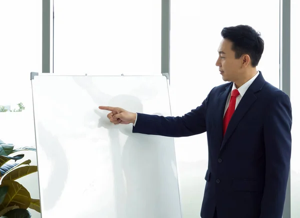 Asian businessman in suit pointing finger at white board. Training and education concepts.