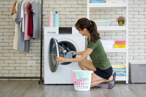 Asyalı ev hanımı çamaşır makinesinden yeni yıkanmış mavi bezi alıyor. Çamaşır odasında çalışma ortamı.