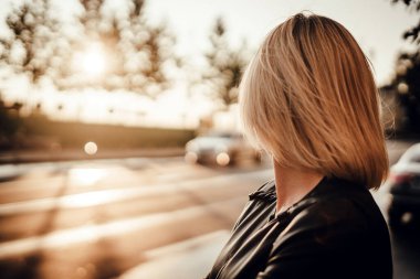 Ceketli genç sarışın bir kızın bulanık portresi duruyor ve şehrin şafağına bakıyor..