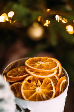 Noel ağacının arka planında bir fincan kurumuş portakal dilimli, çelenk desenli dikey fotoğraf. Noel sıcacık kış havası