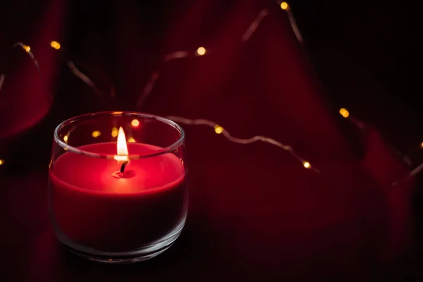 一支红色的香气蜡烛燃烧着 站在红色的背景上 配以来自花环的灯光 圣诞气氛 — 图库照片