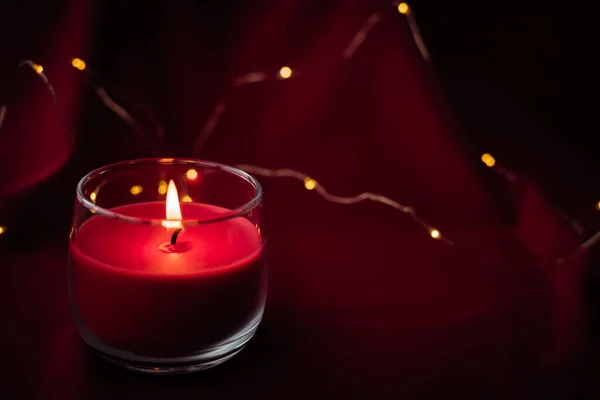 Blurred red aroma candle burns and stands on red background with lights from garlands. Christmas mood — Stock Photo, Image