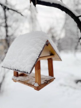 Güzel bir ahşap kuş besleyicisi karda bir ağaca ağırlığını koyar. Yakın plan.