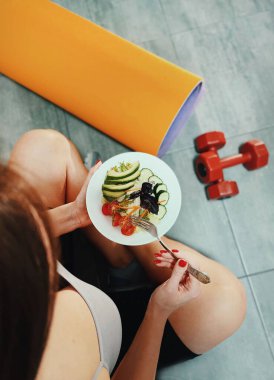 Tabakta sağlıklı salata var. Eğitimden sonra kadın spor paspası ve dambıllarla yerde oturuyor..