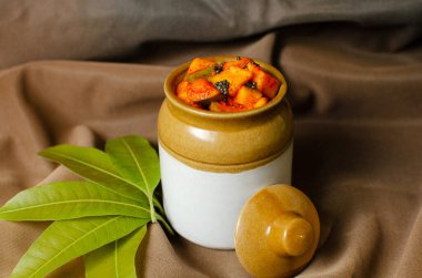 Kahverengi arka planda geleneksel seramik kavanozda ev yapımı çiğ mango turşusu.