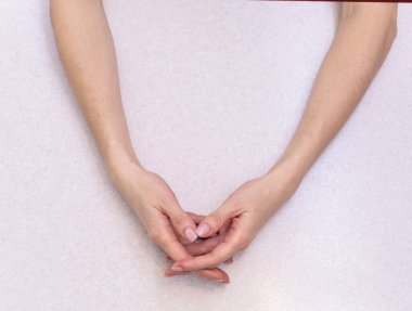 Kızın elleri birbirine dolanmış parmaklarıyla parlak bir masanın üzerinde uzanmış manikürle.
