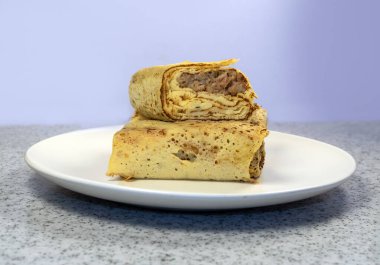 Beyaz tabaktaki etle doldurulmuş gözlemeler, ekşi krema ve mermer tezgahta bir fincan çay..