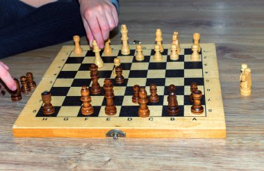 Bilinmeyen birinin elleri. Ahşap zeminde satranç oynayan beyaz bir çocuğun elleri. Kapat..