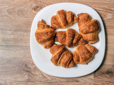 Ahşap masanın üzerindeki büyük beyaz tabakta birkaç ev yapımı kruvasan. Yakın plan. Durgun hayat. Düz yatıyordu