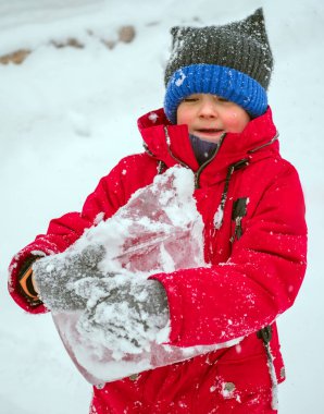 Kırmızı ceketli ve örgü şapkalı beyaz çocuk ellerinde büyük bir buz kalıbı taşıyor..