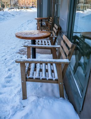 Kışın bir sokak kafesinin masa ve sandalyeleri karla kaplıdır..