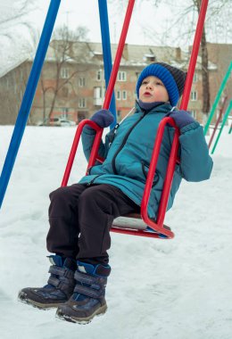 Çocuk kışın salıncakta sallanıyor. Boş kış aktiviteleri. Etkin hafta sonu.