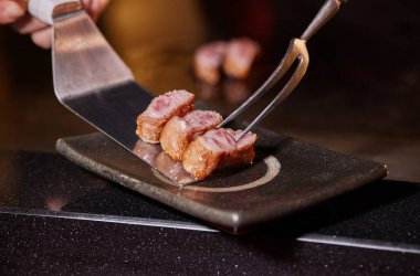 Japon şef Teppanyaki usulü dilimlenmiş lezzetli bir Kobe bifteği veya Wagyu bifteği pişiriyor. Sıcak ve lezzetli biftek, fesa, ranichi