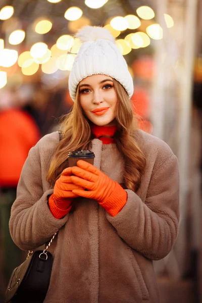 Gadis cantik di latar belakang lampu dengan kopi, di jalan, liburan, tahun baru. berjalan-jalan melalui kota malam — Stok Foto