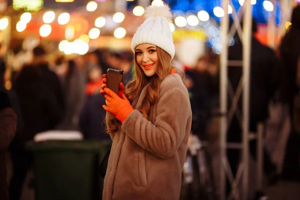 Belle fille sur le fond de lumières avec café, dans la rue, vacances, nouvel an. une promenade dans la ville du soir — Photo