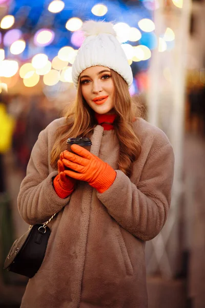 Hermosa chica en el fondo de luces con café, en la calle, vacaciones, año nuevo. un paseo por la ciudad nocturna —  Fotos de Stock