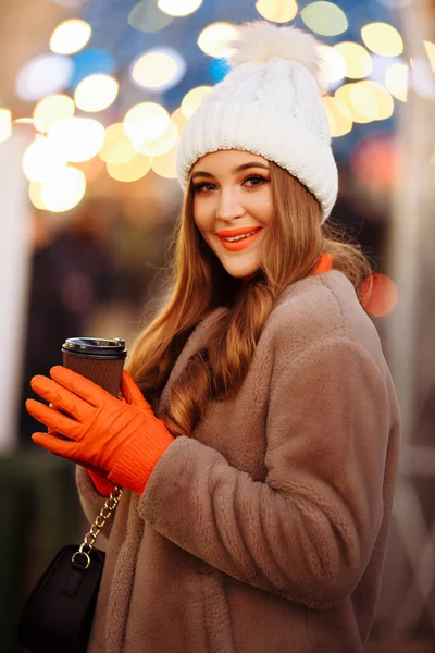 Menina bonita no fundo das luzes com café, na rua, feriado, ano novo. um passeio pela cidade da noite — Fotografia de Stock
