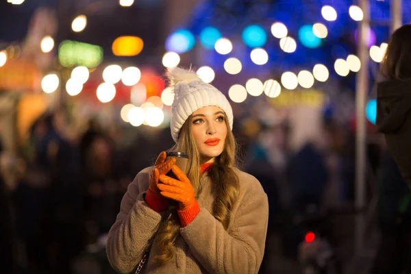 조명을 배경으로 아름다운 소녀가 커피를 마시고 거리에서 휴가를 보내고 새해를 맞이 합니다. 밤에 산책하는 도시 — 스톡 사진