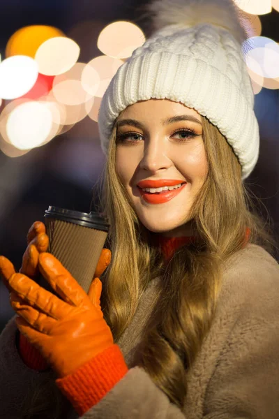 Menina bonita no fundo das luzes com café, na rua, feriado, ano novo. um passeio pela cidade da noite — Fotografia de Stock