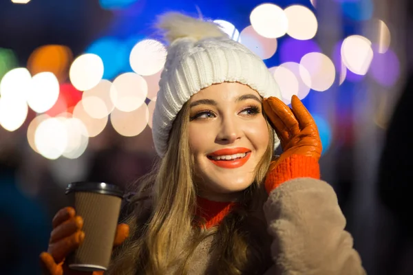 Mooi meisje op de achtergrond van lichten met koffie, op straat, vakantie, nieuwjaar. een wandeling door de avondstad — Stockfoto