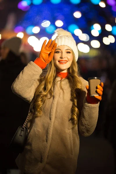 Vacker flicka på bakgrunden av ljus med kaffe, på gatan, semester, nytt år. en promenad genom kvällsstaden — Stockfoto