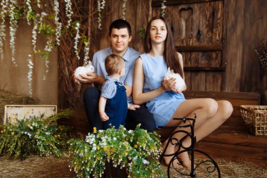 Köydeki aile, kollarında tavşanlarla. Anne ve babasının yanında küçük bir çocuk. Beyaz tavşanlar