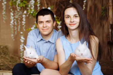 Bir adam ve bir kız ellerinde beyaz tavşanlar tutuyorlar.