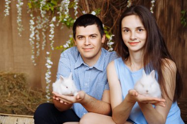 Bir adam ve bir kız ellerinde beyaz tavşanlar tutuyorlar.