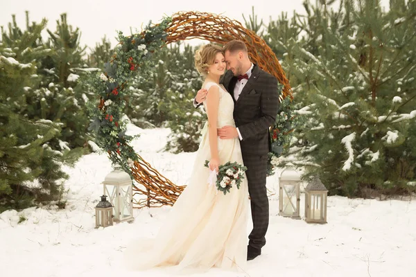 Le couple est câlin et proche du baiser, tenant la main, un bouquet dans leurs mains. Un costume avec un papillon et un manteau avec une robe. La mariée et le marié — Photo