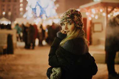 Kış şapkalı güzel bir kız Noel ağacının yanında, kış tatilleri, tatiller ve bir film fotoğrafının altında buğdayla yürüyor.