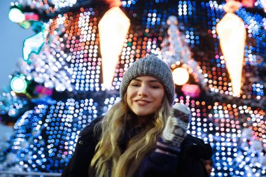 Kış şapkalı güzel bir kız Noel ağacının yanında, kış tatilleri, tatiller ve bir film fotoğrafının altında buğdayla yürüyor.