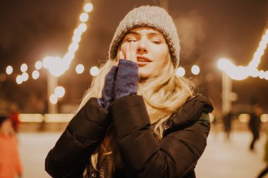 Kış şapkalı güzel bir kız Noel ağacının yanında, kış tatilleri, tatiller ve bir film fotoğrafının altında buğdayla yürüyor.