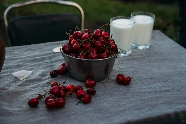 Sweet cherries and two glasses of milk stand on a table on a street in a village Stock Image